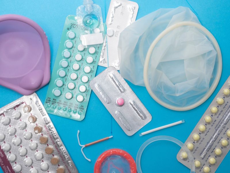 różne rodzaje antykoncepcji - prezerwatywy, tabletki antykoncepcyjne, wkładki dopochwowe, leżą na niebieskim blacie. 
